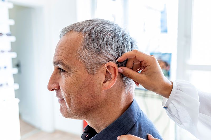 Doctor fitting a hearing aid unto patient