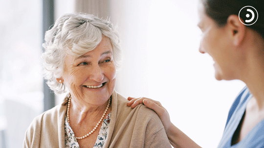 Senior woman and nurse smiling toward each other.