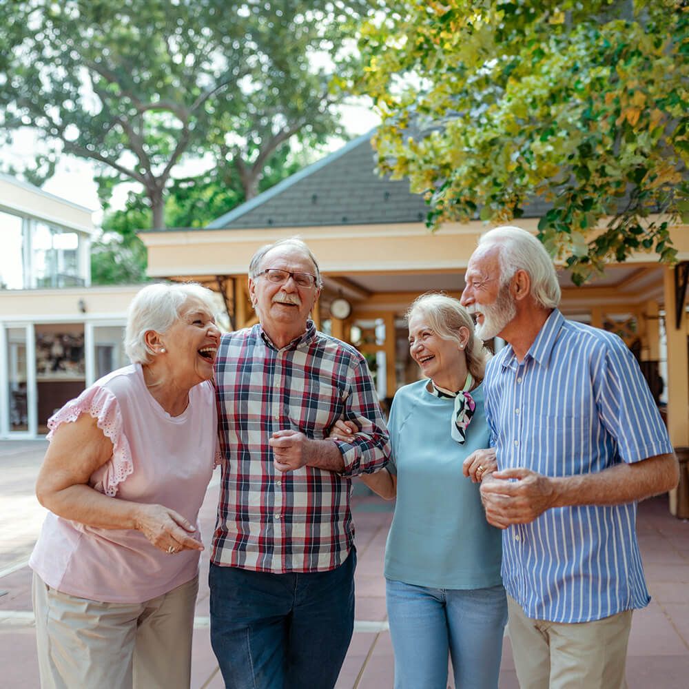 Four elderly individuals walking together outside, laughing and enjoying each other’s company.