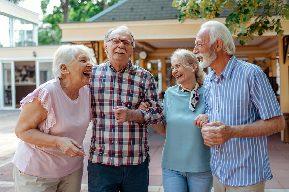 Four elderly individuals walking together outside, laughing and enjoying each other’s company.