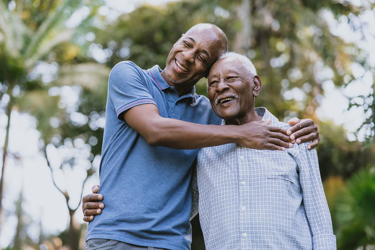 Father and son laughing together in an affectionate hug Elderly father laughing joyfully as his adult son hugs him lovingly